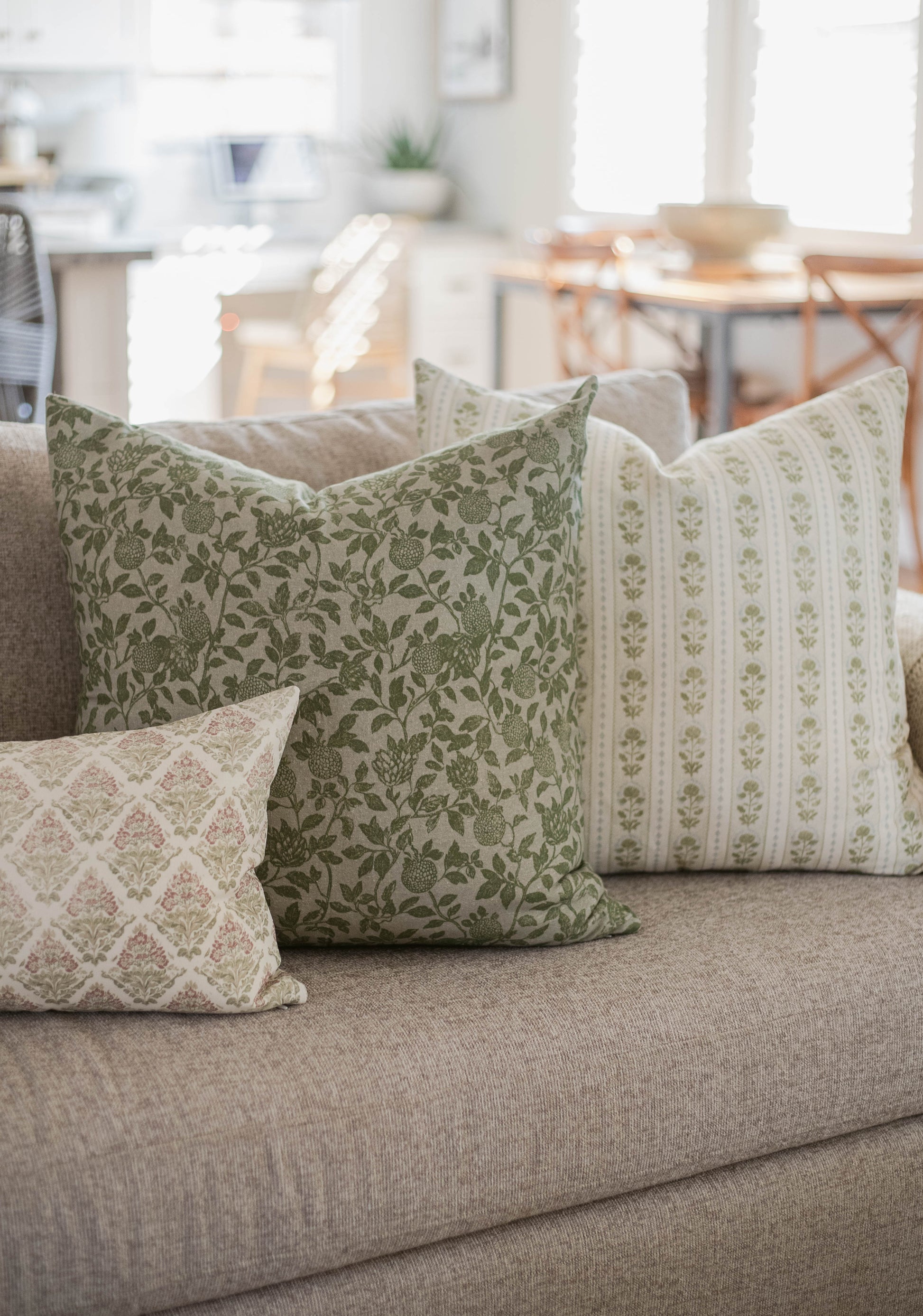 Green and cream patterned throw pillows with floral and striped designs on a gray upholstered sofa.
