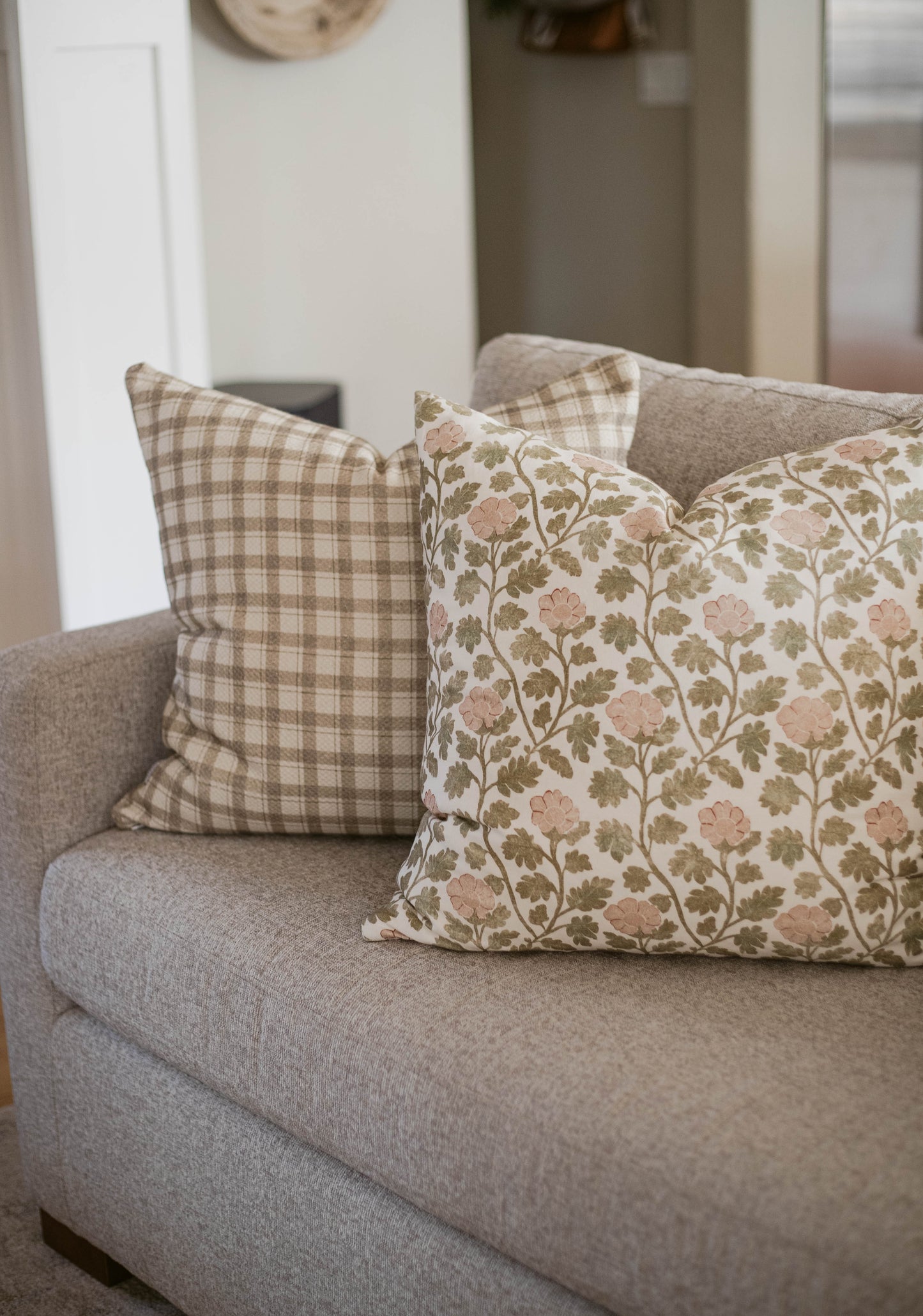 Two cotton throw pillows on a gray sofa: one with beige plaid pattern, one with pink flowers and green foliage.