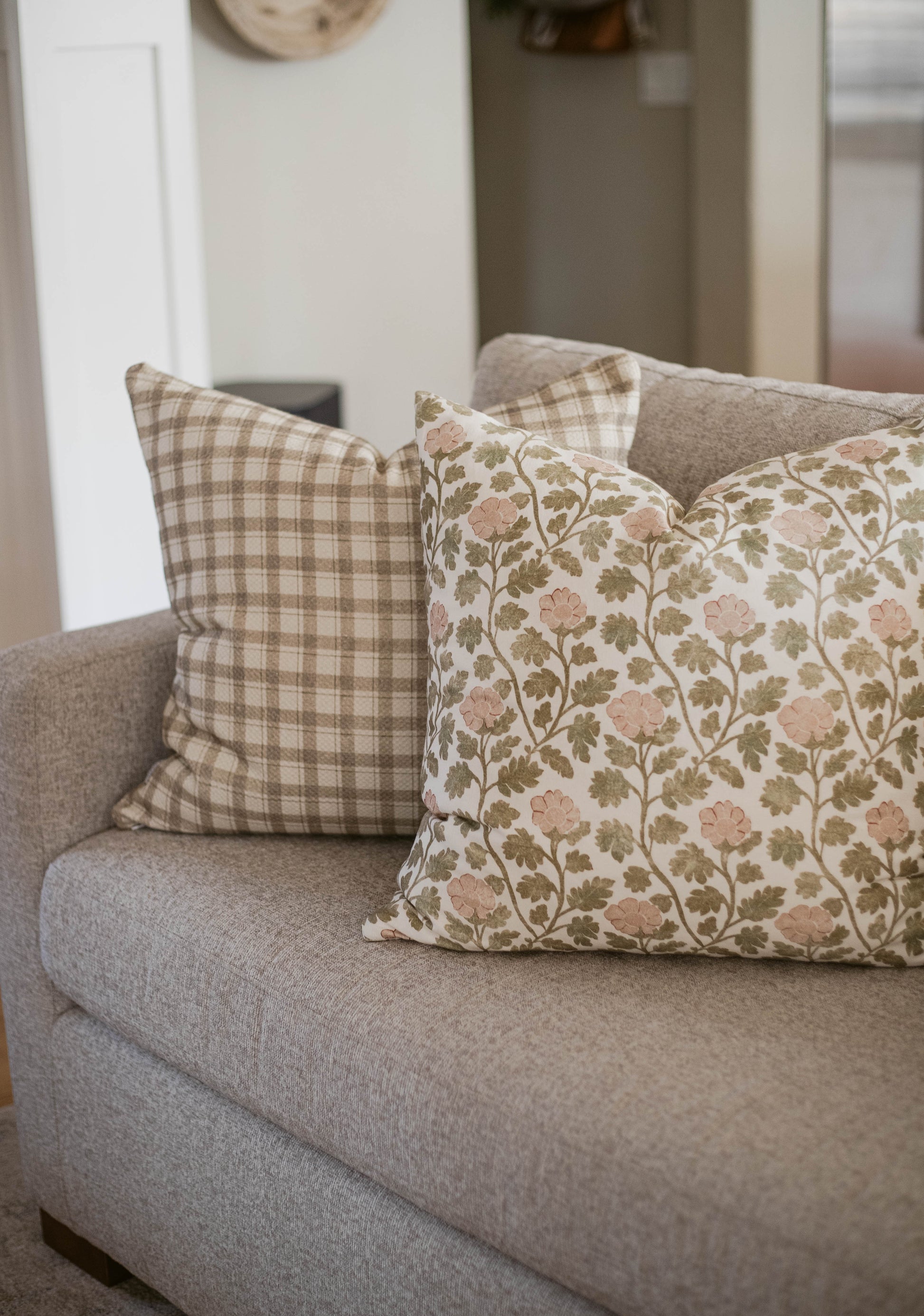 Two cotton throw pillows on a gray sofa: one with beige plaid pattern, one with pink flowers and green foliage.