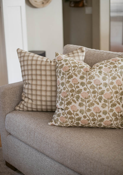 Two cotton throw pillows on a gray sofa: one with beige plaid pattern, one with pink flowers and green foliage.