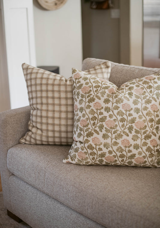 Two cotton throw pillows on a gray sofa: one with beige plaid pattern, one with pink flowers and green foliage.
