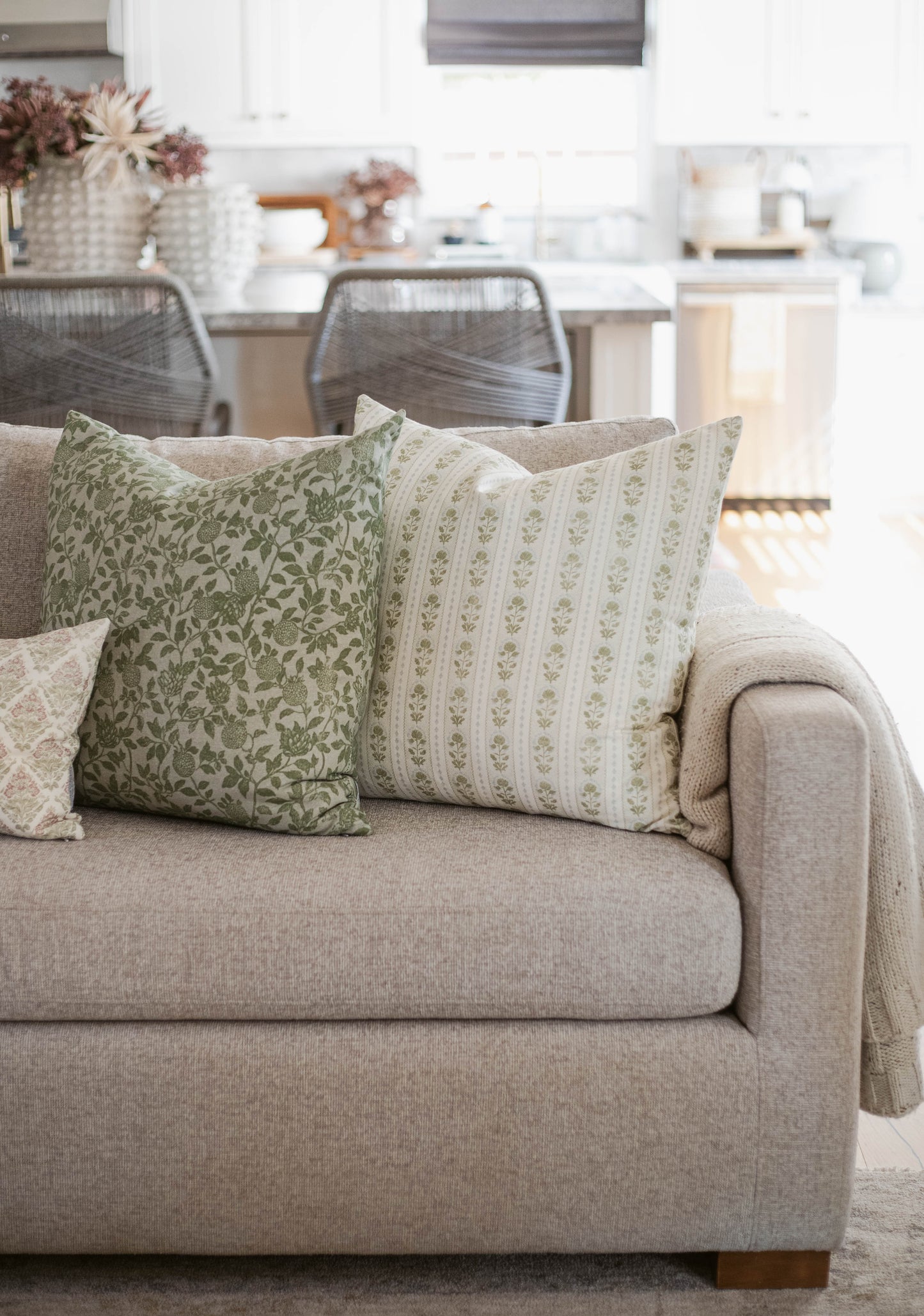 Five decorative pillows in varying sizes with green floral and striped patterns arranged on a beige sofa.