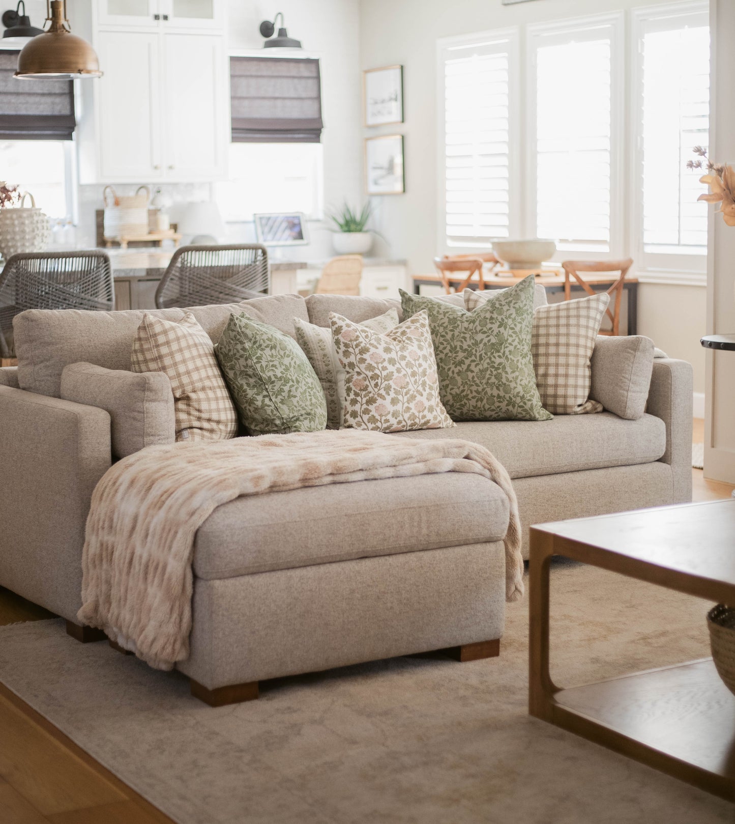 Beige upholstered sectional sofa with green and cream patterned pillows in bright living room setting.