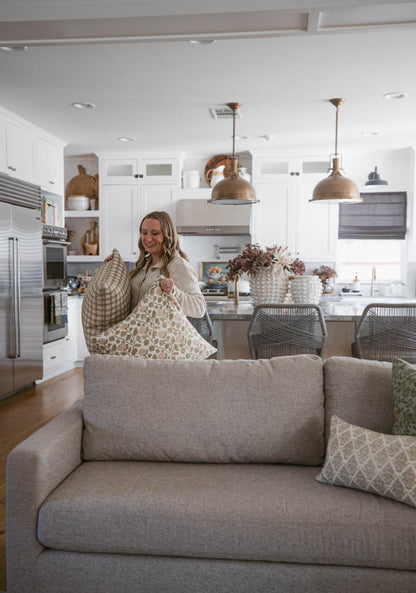 Woman holding patterned and checkered decorative pillows while sitting on a gray sofa in a modern kitchen.