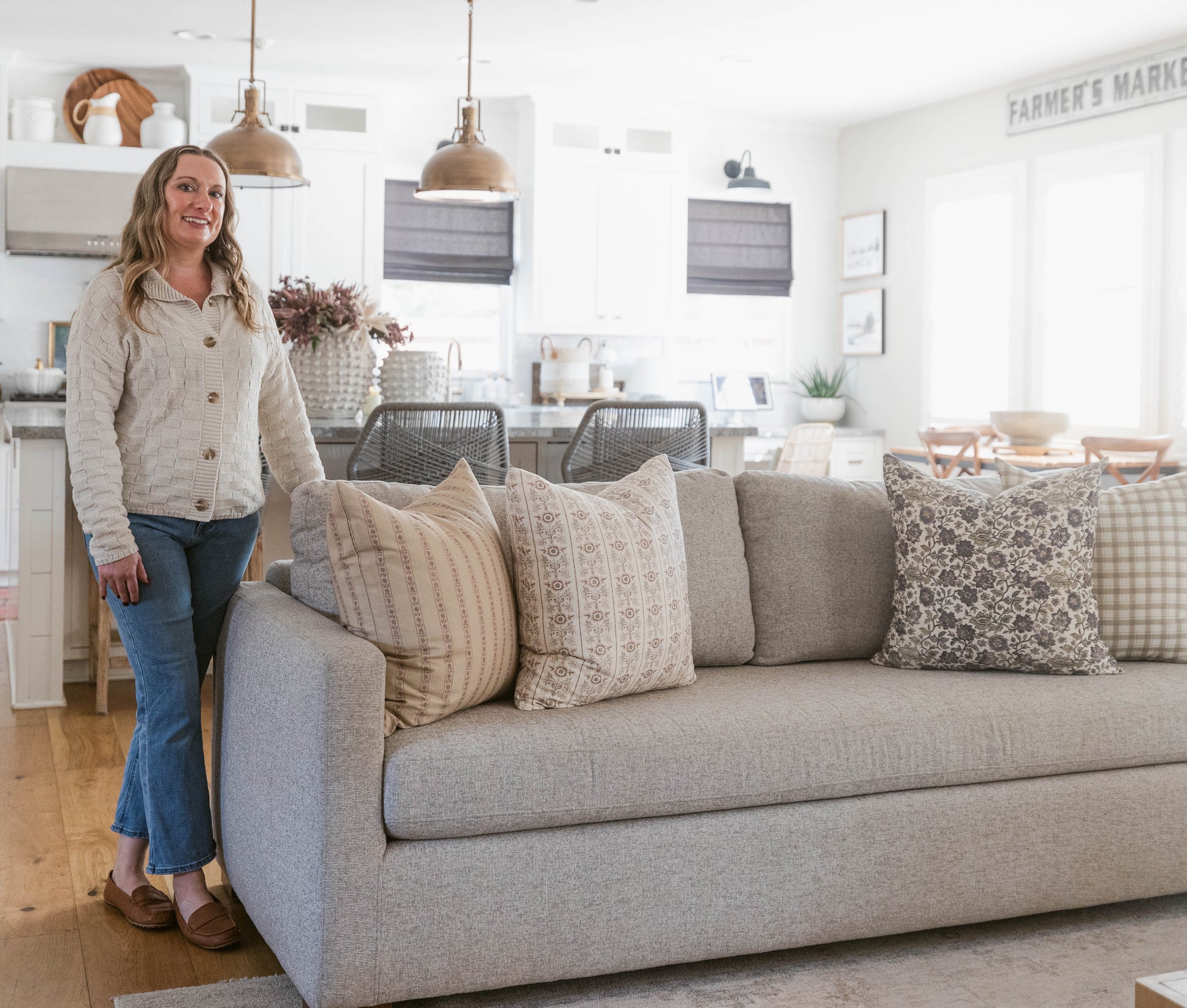 Beige upholstered sofa with decorative pillows in neutral patterns, displayed in a bright farmhouse-style living room.