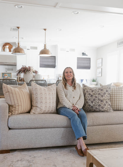Four decorative pillows with striped, geometric, and floral patterns in neutral tones displayed on a beige sofa.