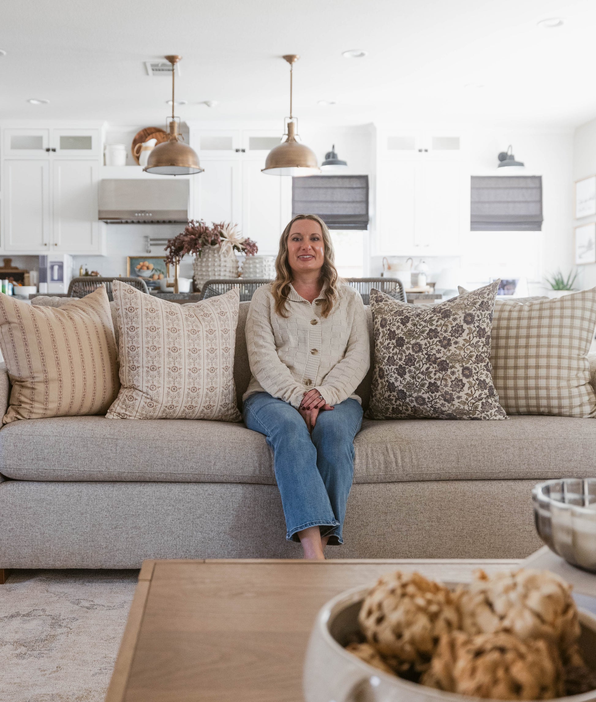 Beige upholstered sofa with patterned throw pillows in a bright kitchen and living room setting.