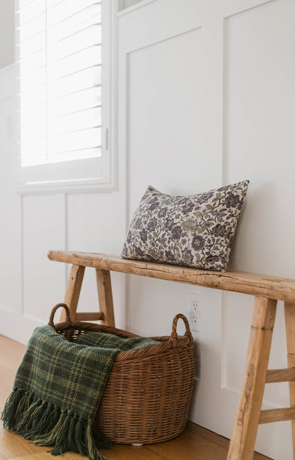 Blank framed canvas hanging on white wall above wooden bench with patterned pillow and wicker basket.