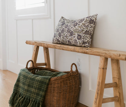 Hattie pillow with gray floral damask pattern displayed on wooden bench next to wicker basket with green throw blanket.