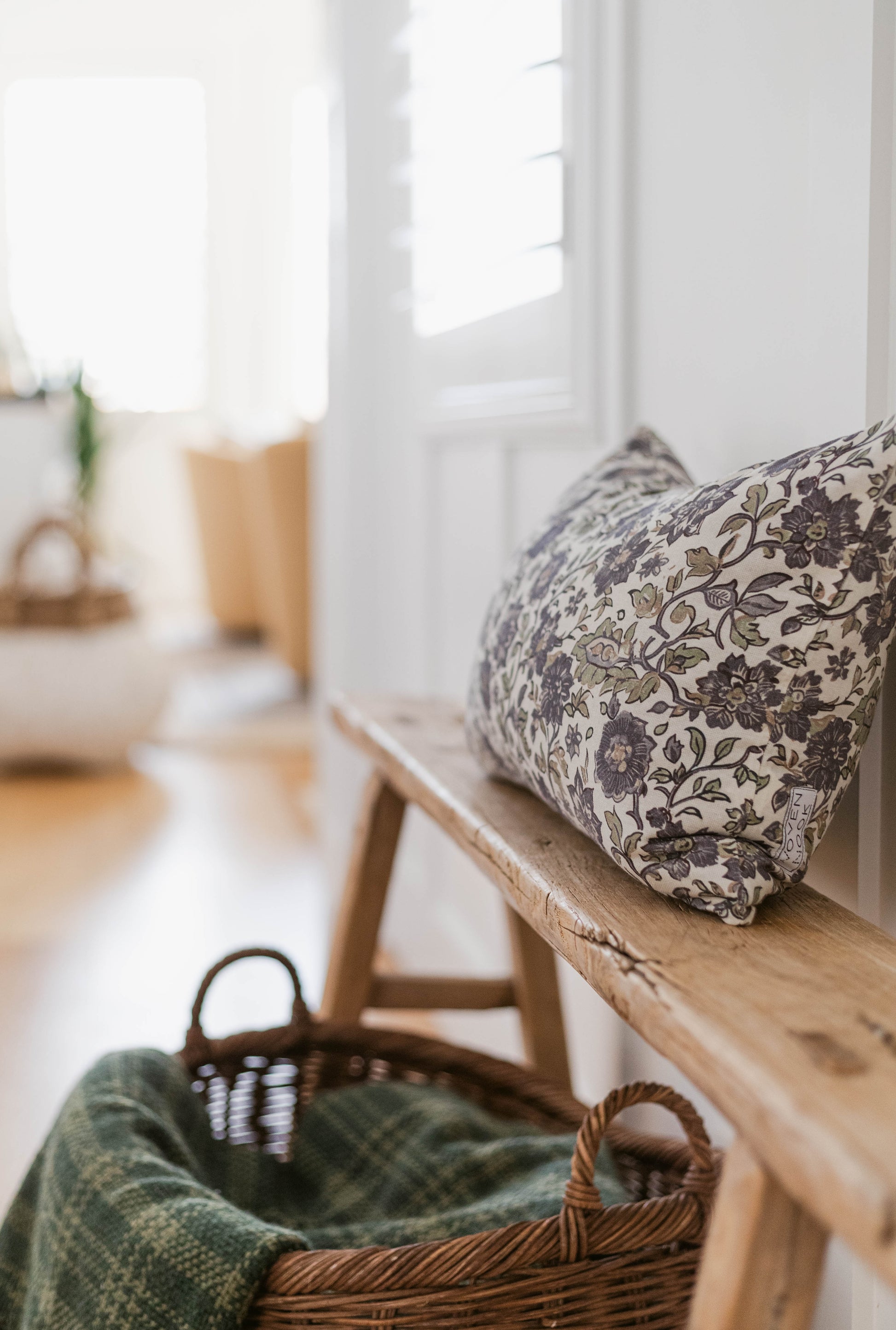 Rectangular pillow with dark floral pattern on cream fabric, resting on wooden window seat.