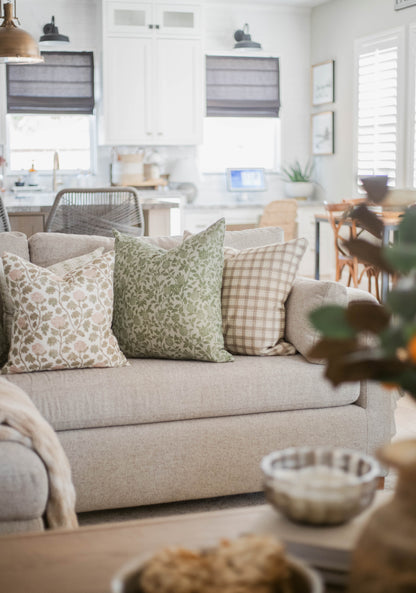 Three decorative pillows on beige sofa: floral print, green leaf pattern, and beige gingham check.
