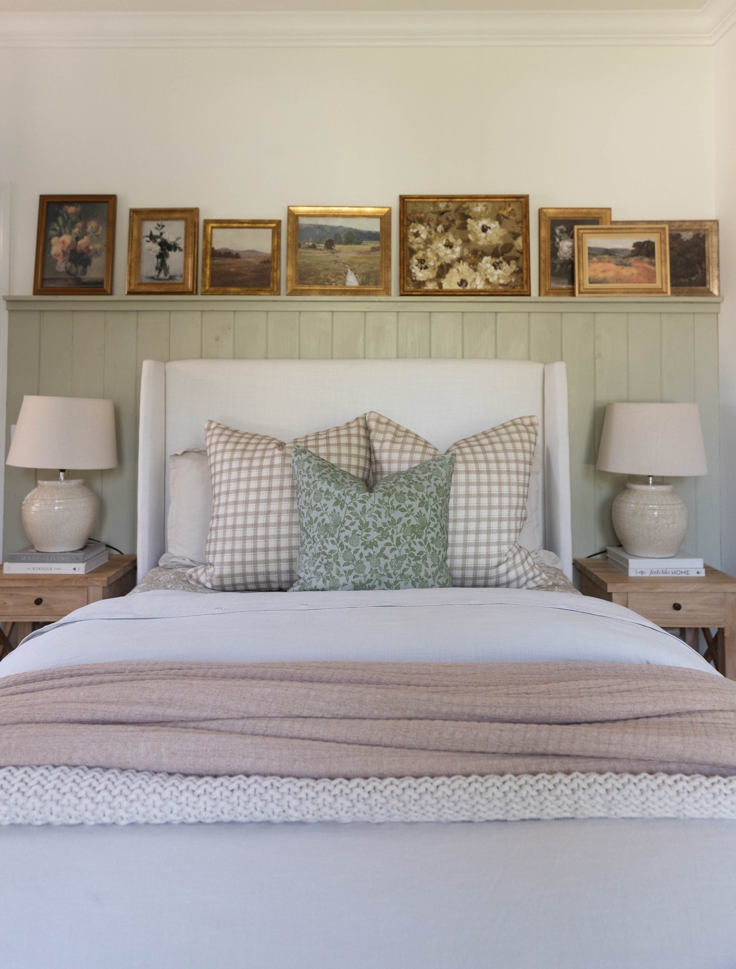 White upholstered bed with gingham and leaf-patterned pillows, flanked by wood nightstands with ceramic lamps.