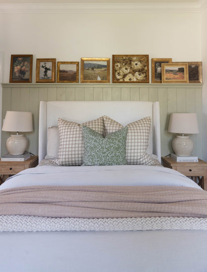 White upholstered bed with gingham and leaf-patterned pillows, flanked by wood nightstands with ceramic lamps.
