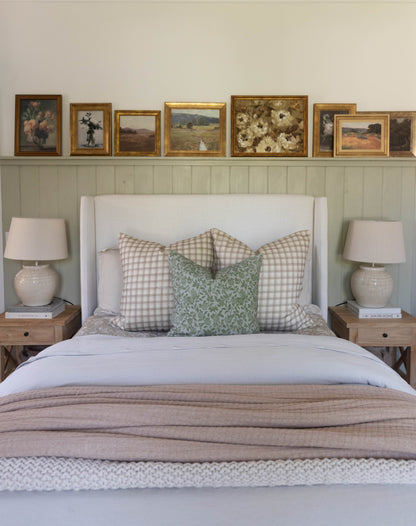 Beige and green patterned throw pillow displayed on a bed with gingham and floral cushions.