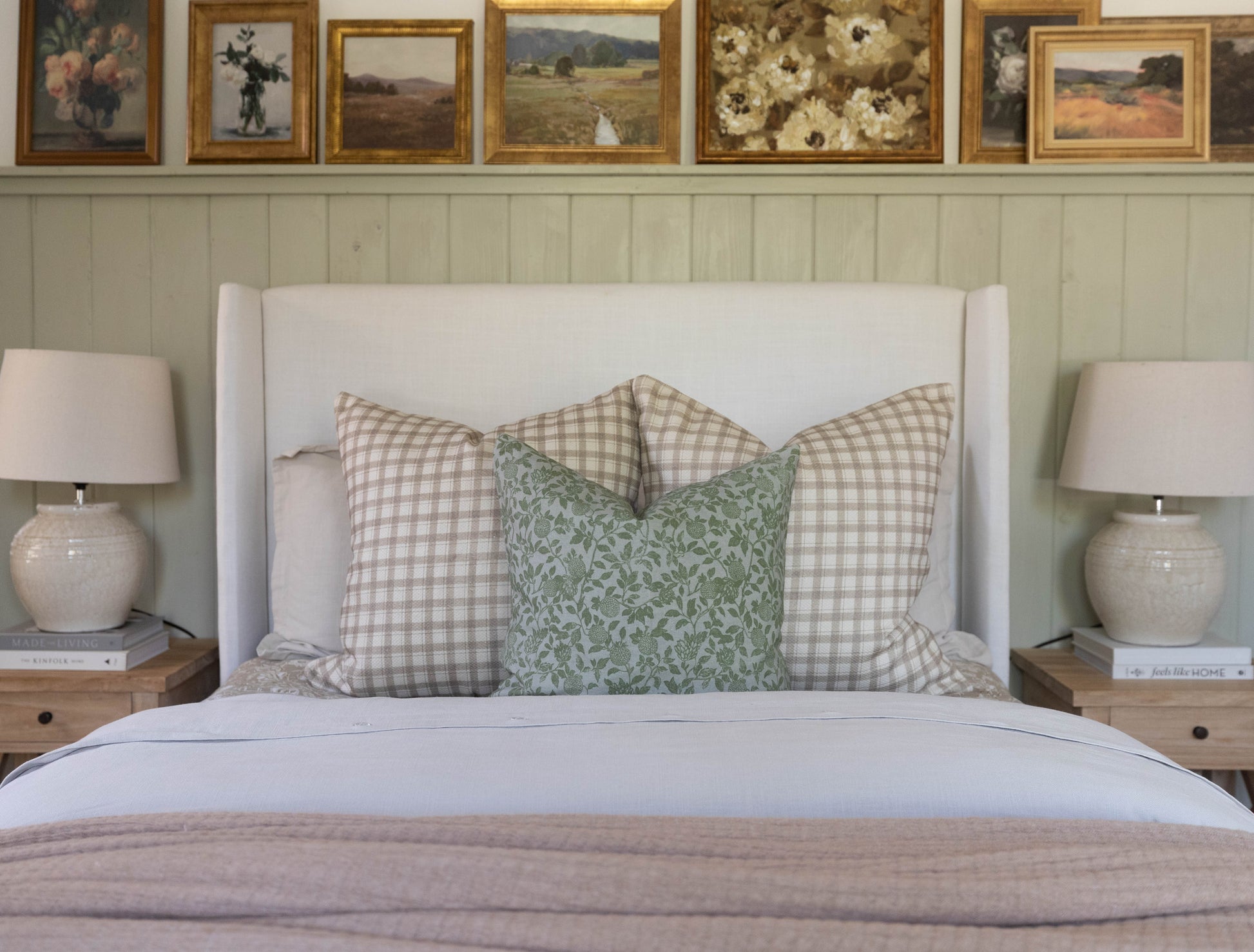 Green floral lumbar pillow displayed on bed with gingham throw pillows and white headboard.