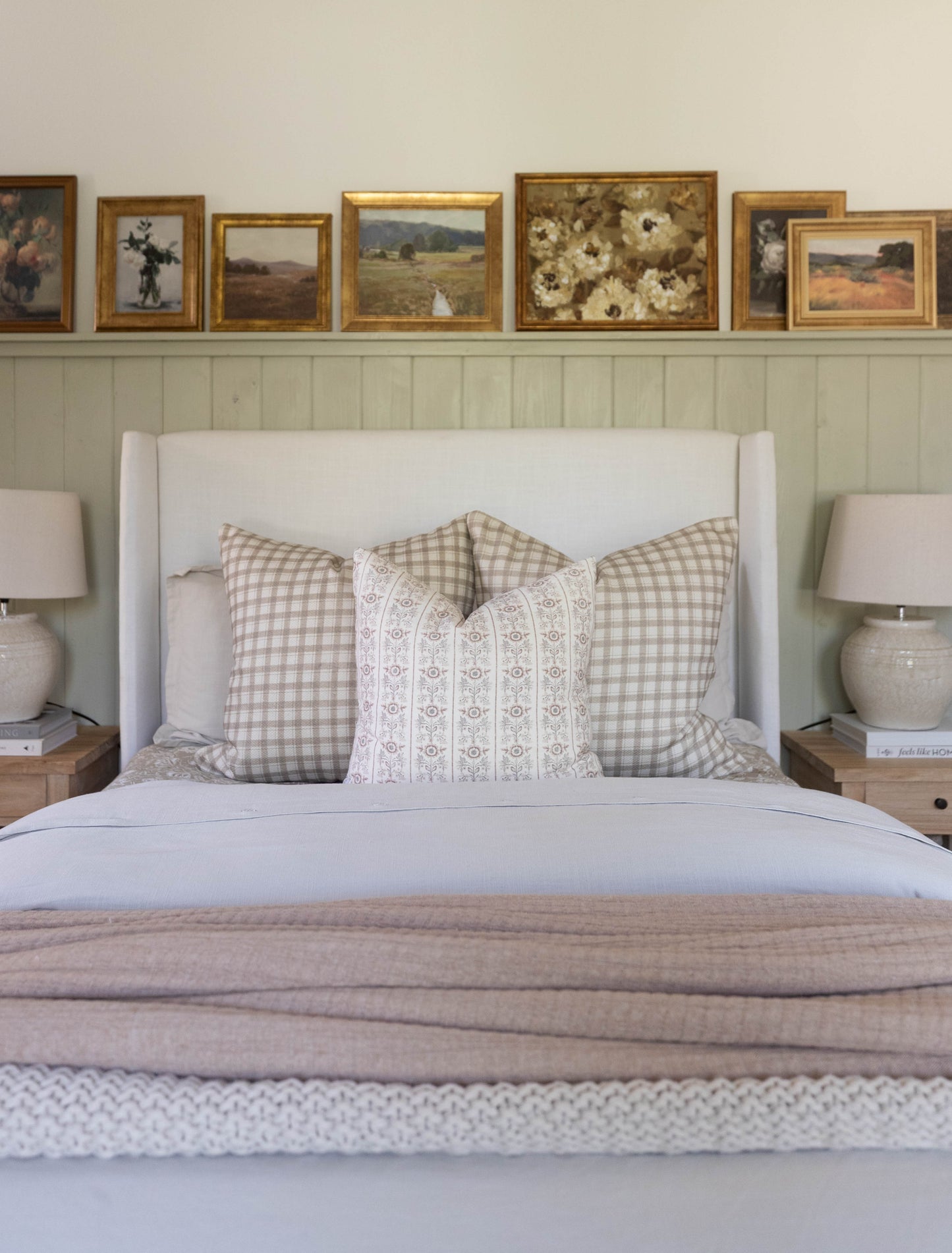 White upholstered bed with wingback headboard, dressed with gingham and patterned pillows and neutral bedding.