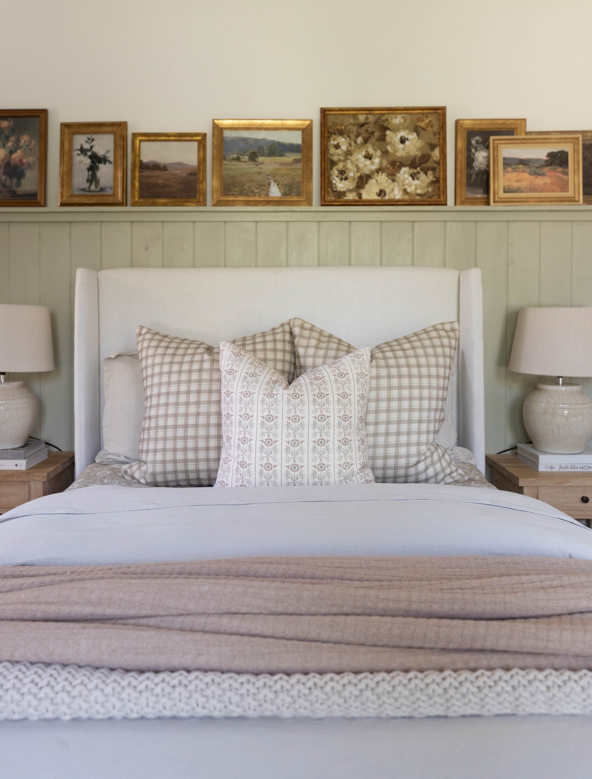 White upholstered bed with wingback headboard, dressed with gingham and patterned pillows and neutral bedding.
