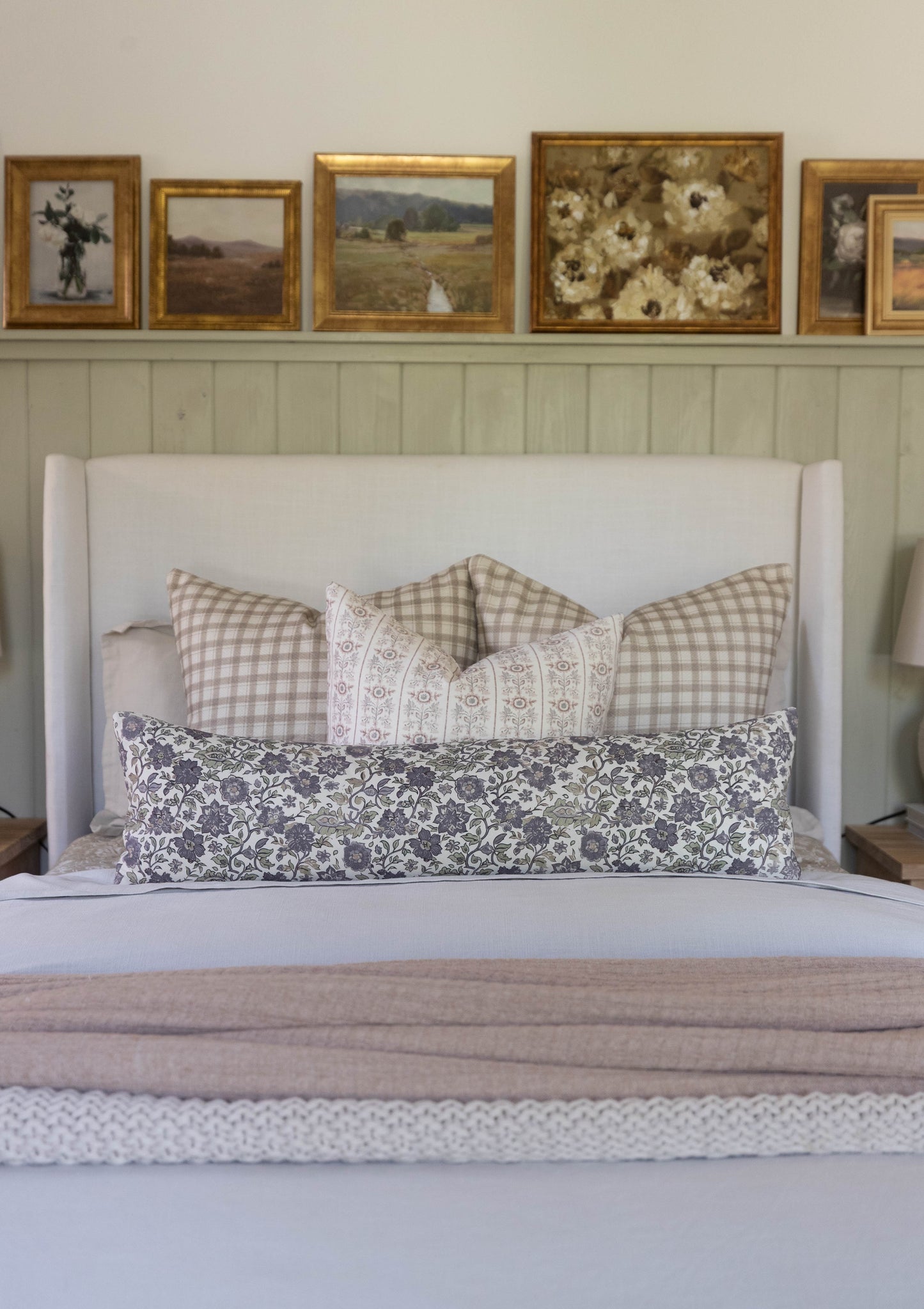 White upholstered bed headboard styled with patterned and checkered decorative pillows and folded linens.