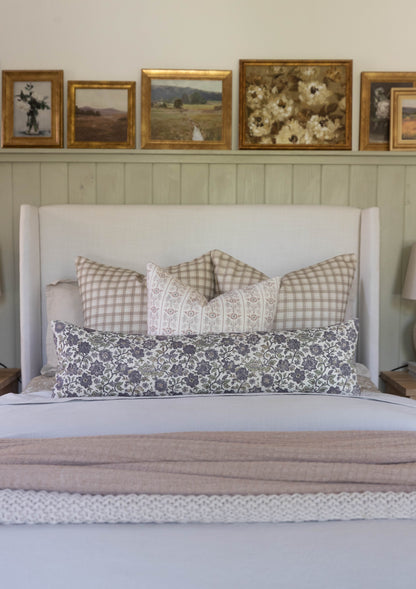 White upholstered bed headboard styled with patterned and checkered decorative pillows and folded linens.