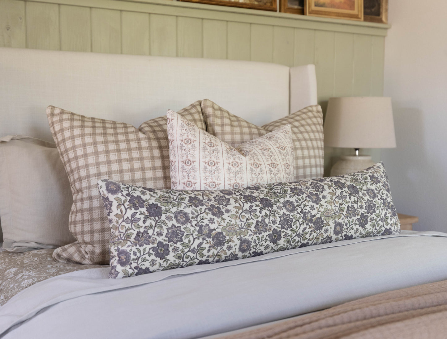 Decorative pillows in beige gingham, cream floral, and blue damask patterns arranged on a bed with white headboard.