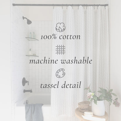 Cream cotton shower curtain with woven texture and tassel trim hung on gray rod in white tile bathroom.