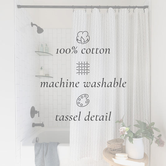 Cream cotton shower curtain with woven texture and tassel trim hung on gray rod in white tile bathroom.