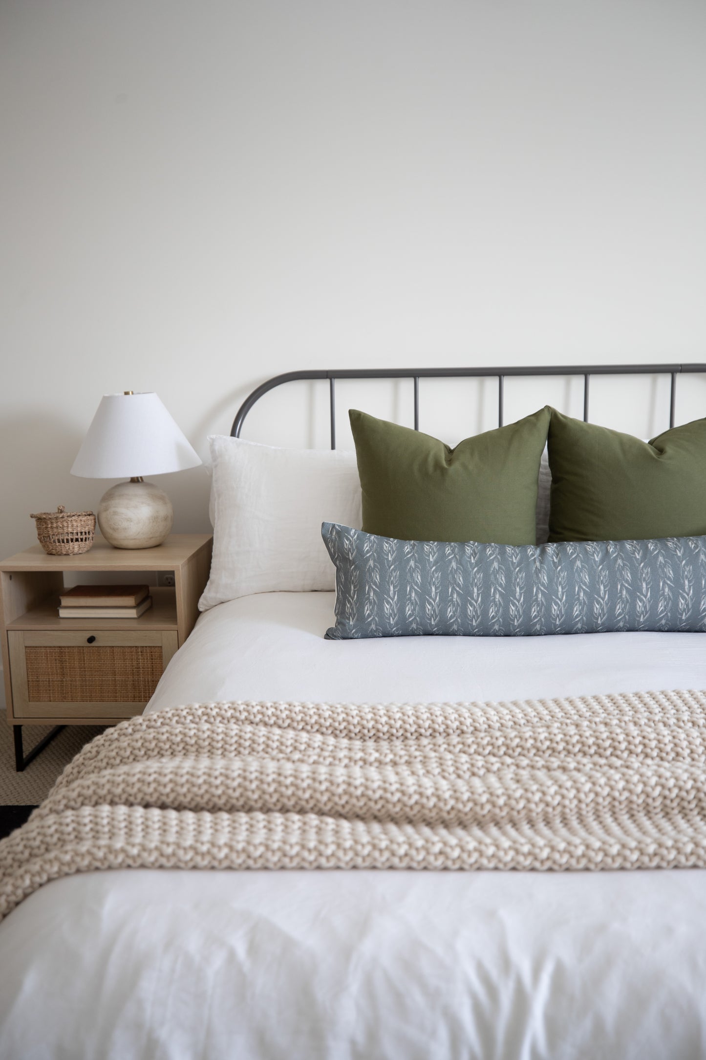 Sage green lumbar pillow with leaf pattern displayed on bed with white and cream pillows.