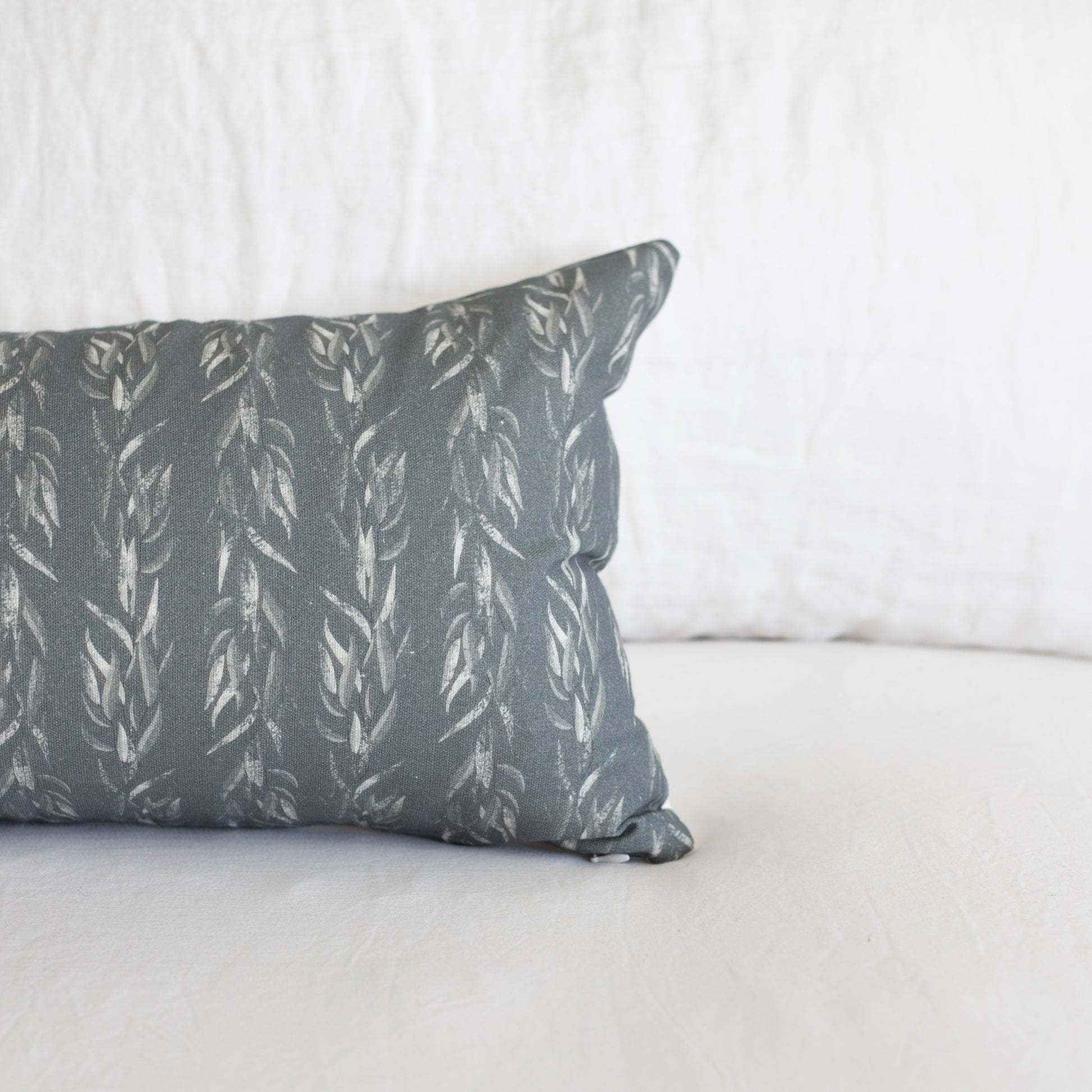 Rectangular lumbar pillow with sage green fabric featuring an all-over leaf pattern in cream.
