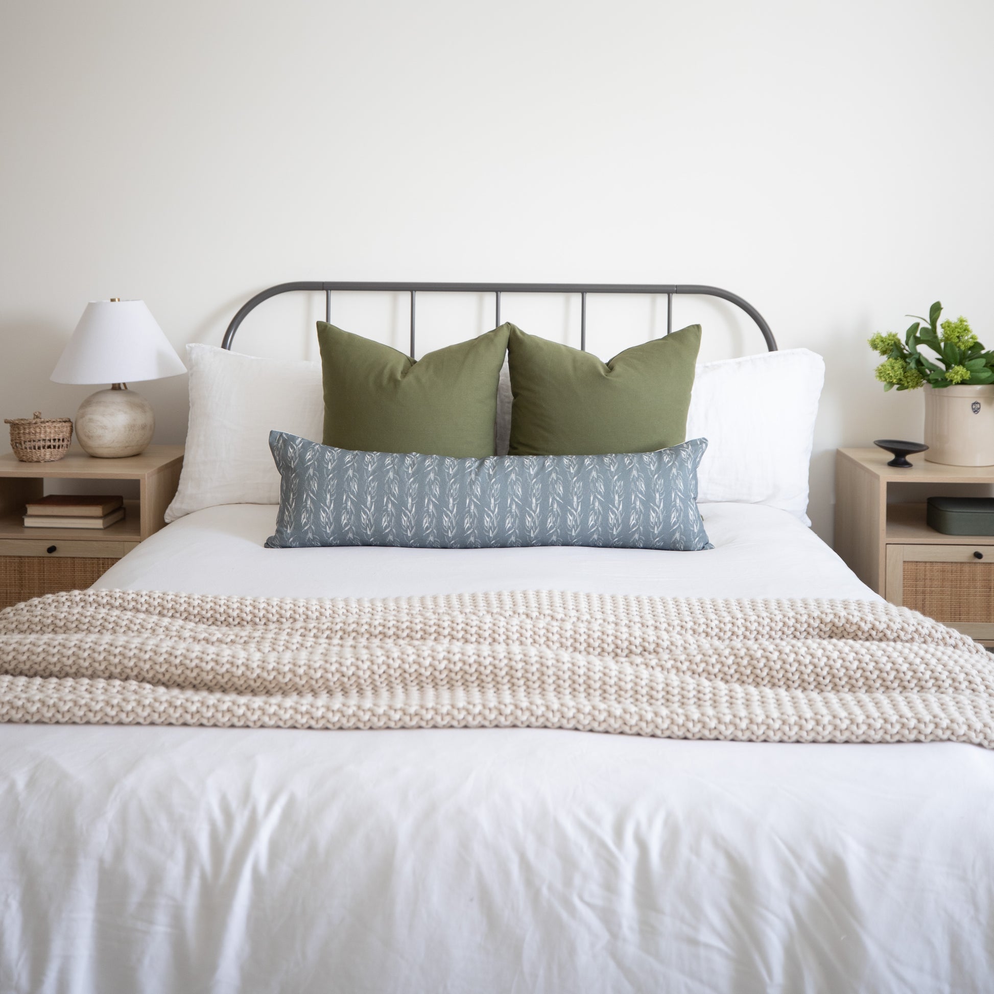 Sage green lumbar pillow with solid fabric displayed on bed between white and patterned pillows.