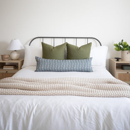 Sage green lumbar pillow with solid fabric displayed on bed between white and patterned pillows.