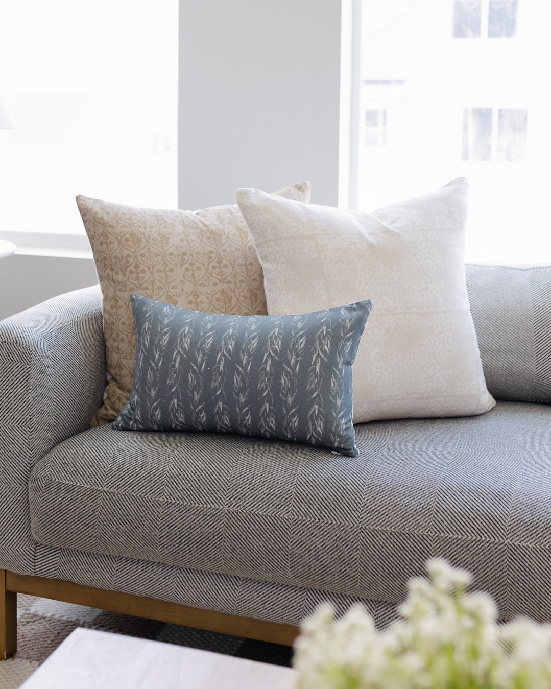 Blue-gray rectangular pillow with faded leaf pattern, displayed on gray sofa with coordinating throw pillows.