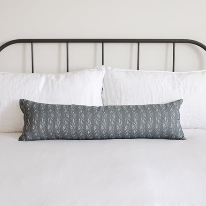 Sage green lumbar pillow with repeating leaf pattern displayed on bed with white pillows and black metal headboard.