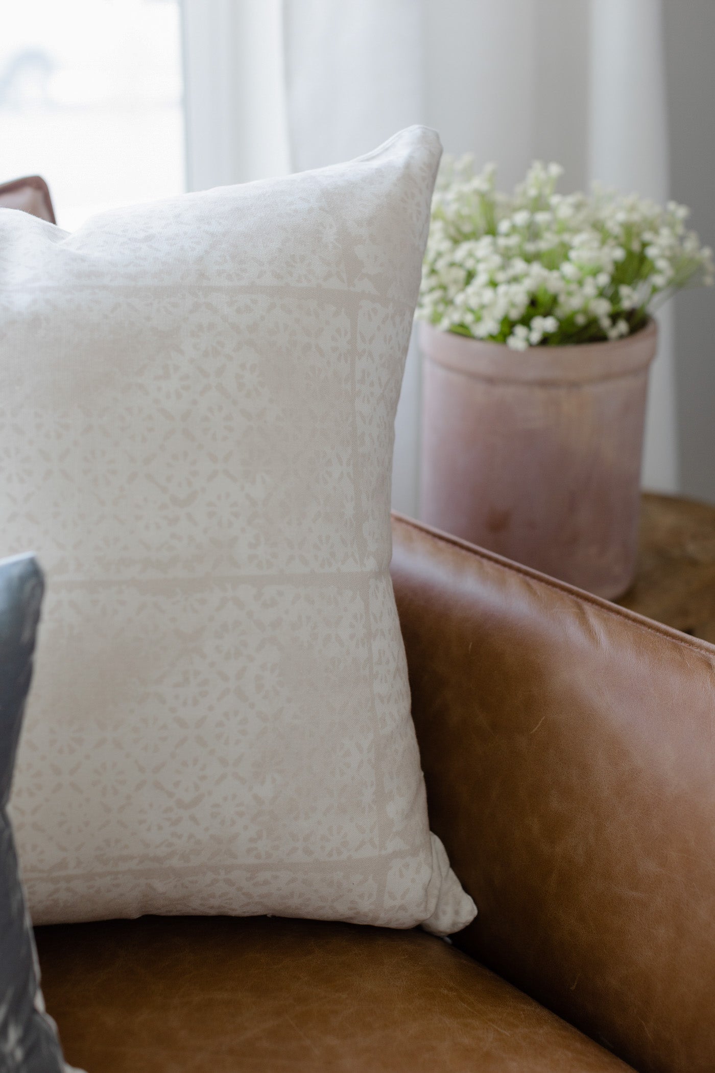 Cream-colored pillow with faded floral pattern displayed on brown leather furniture.