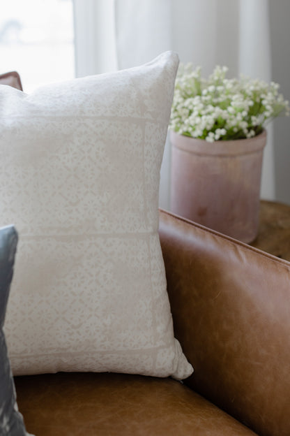 Cream-colored pillow with faded floral pattern displayed on brown leather furniture.