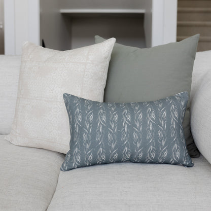 Rectangular pillow with faded leaf pattern in slate blue and cream, displayed on a light gray sofa with coordinating solid pi