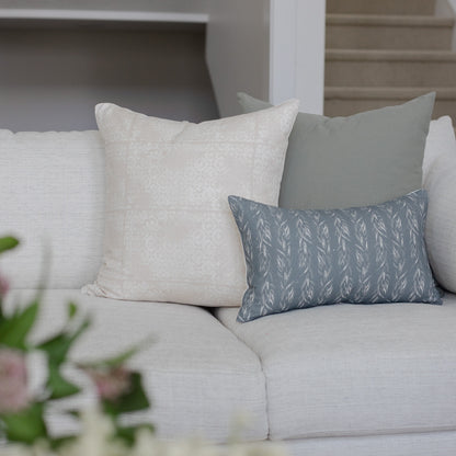 Blue-gray rectangular pillow with faded leaf pattern displayed on light gray sofa with solid pillows.