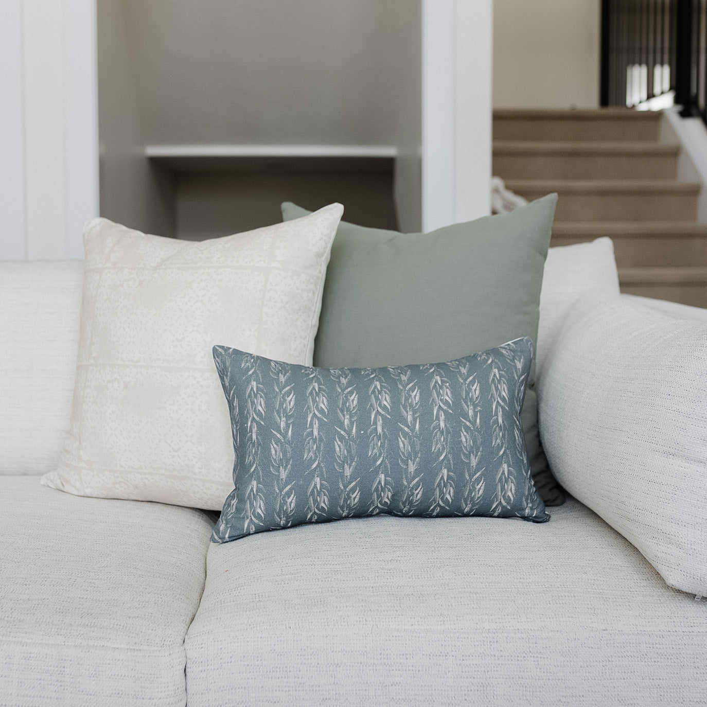 Blue-gray lumbar pillow with white leaf pattern displayed on cream sofa with neutral pillows.