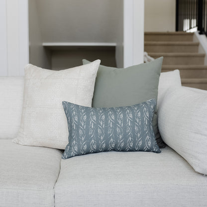 Blue-gray lumbar pillow with white leaf pattern displayed on cream sofa with neutral pillows.