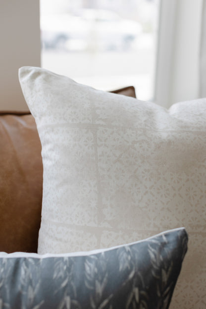 Cream linen pillow with faded floral pattern, displayed on brown leather furniture.