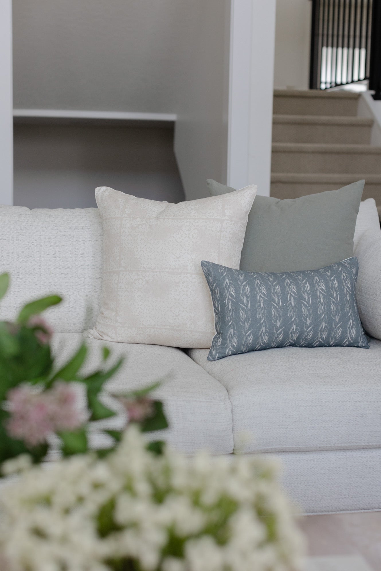 Blue-gray lumbar pillow with repeating leaf pattern displayed on light gray sofa.