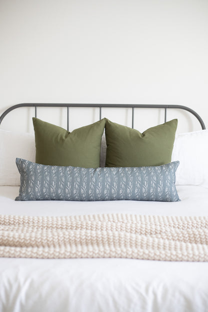 Sage green solid lumbar pillow styled with coordinating leaf-patterned pillow on a metal bed frame.