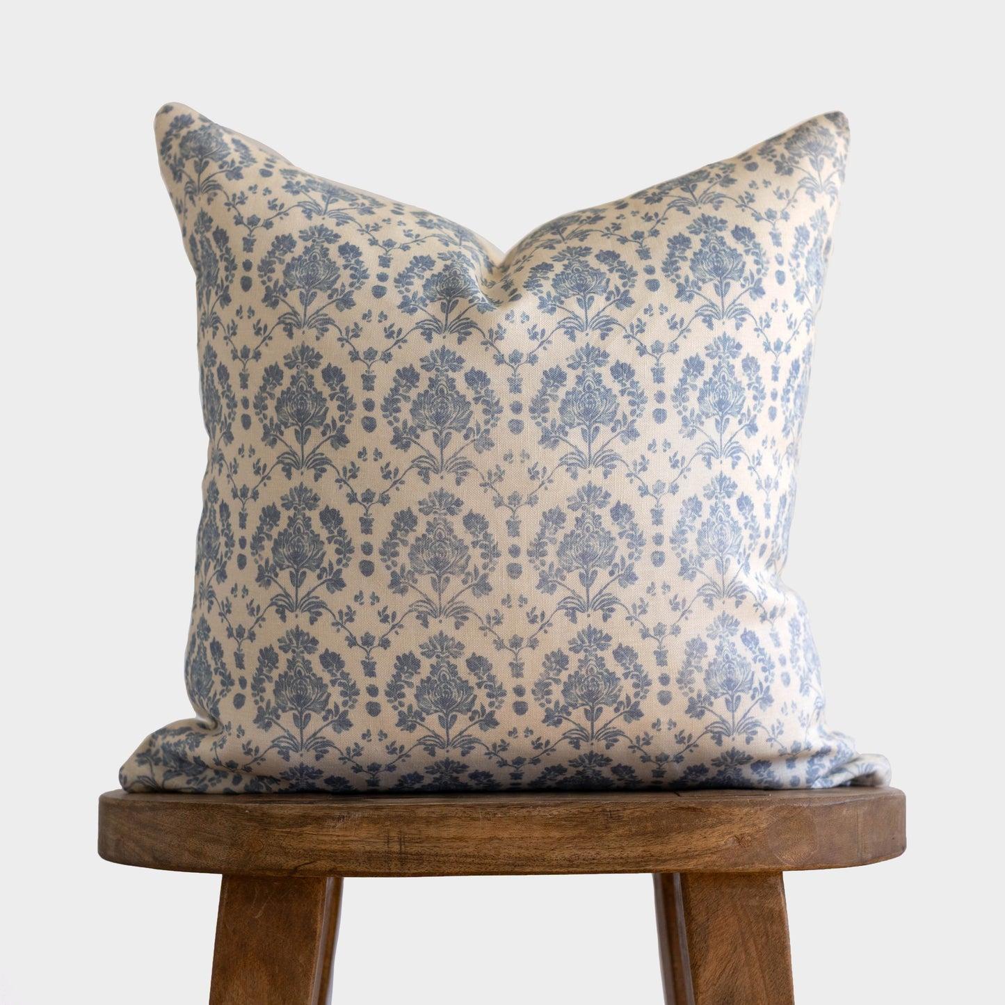 Blue and cream damask patterned linen pillow with pointed corners displayed on wooden stool.