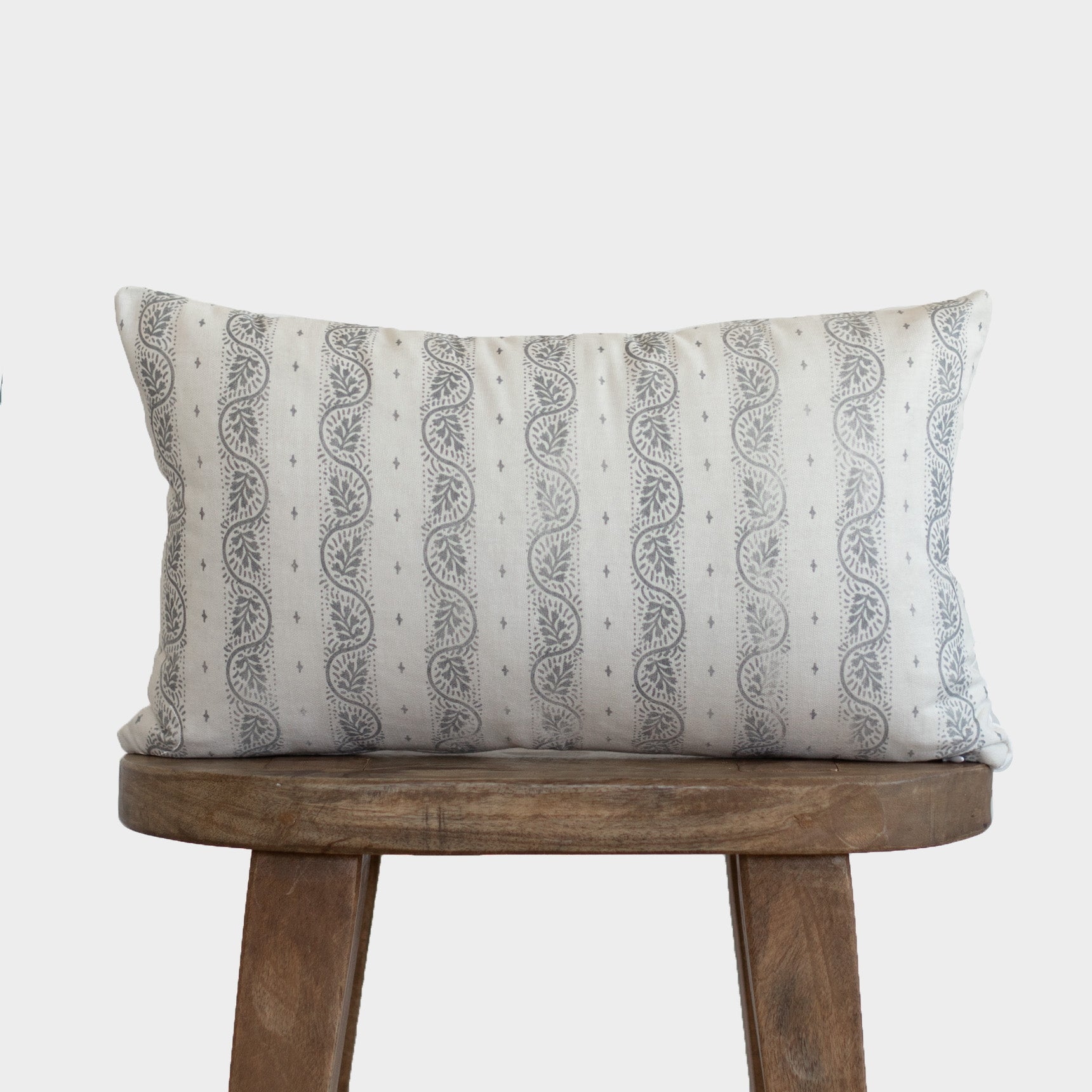 Rectangular lumbar pillow with cream background and gray vertical striped pattern with leaf motifs, displayed on wooden stool