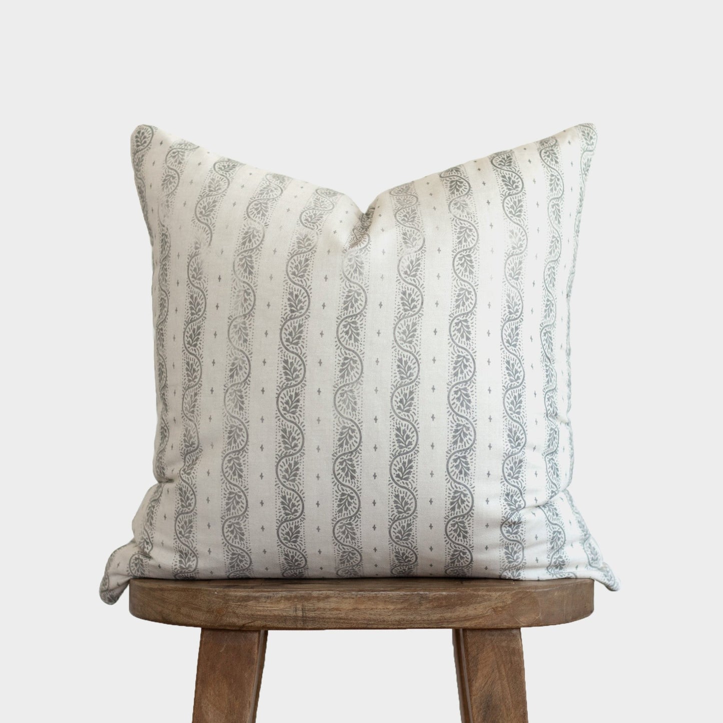 Cream throw pillow with gray paisley stripe pattern displayed on wooden stool.