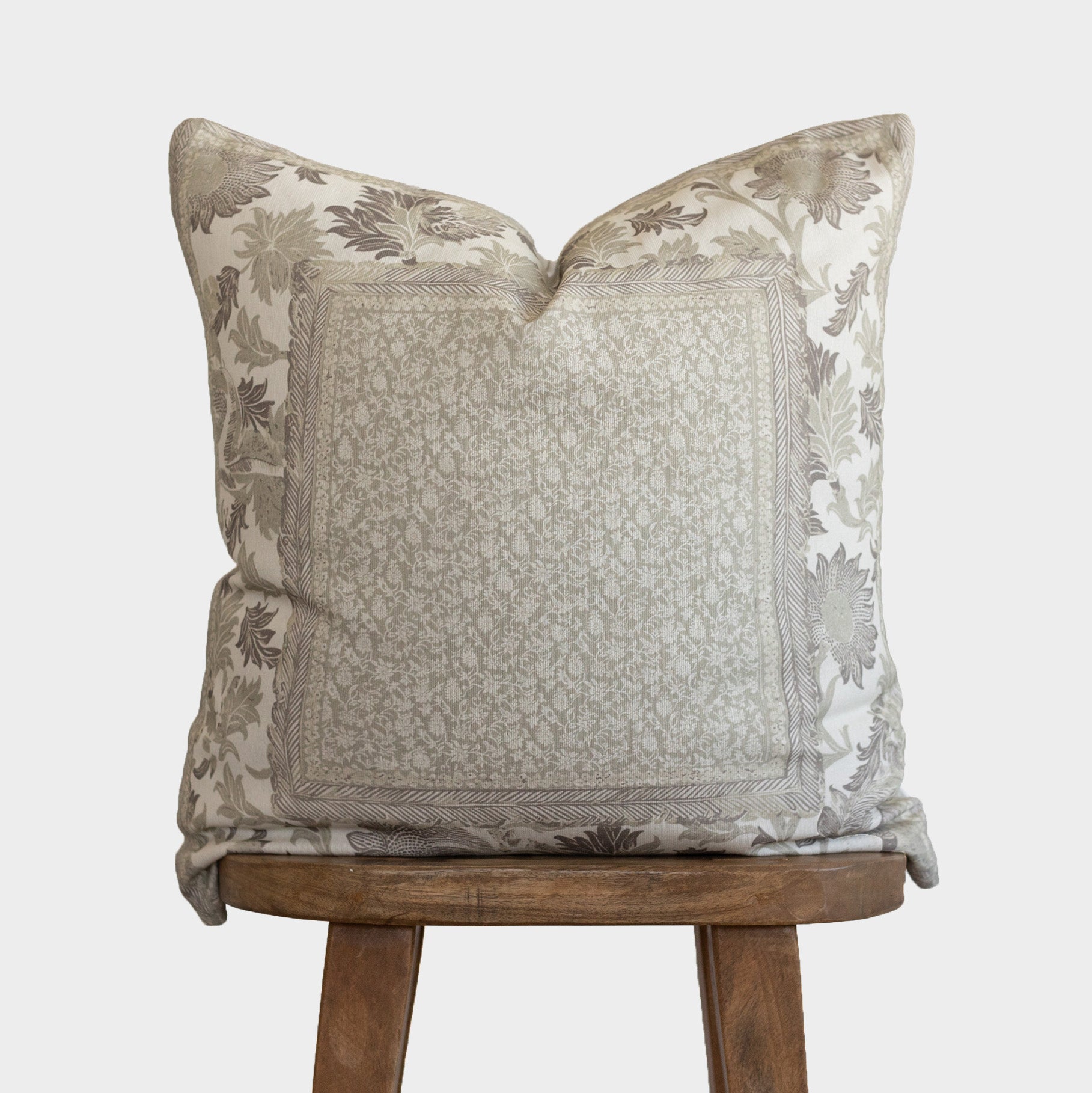 Corduroy pillow with botanical print border in cream and taupe tones, displayed on wooden stool.