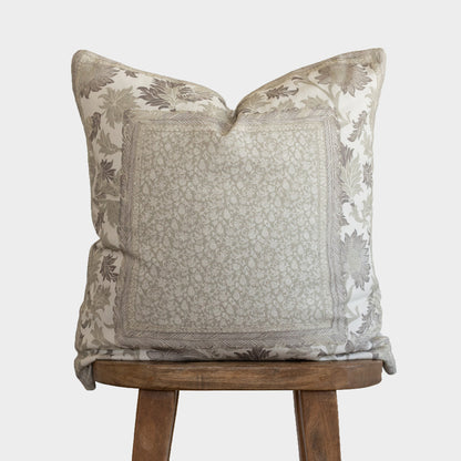 Corduroy pillow with botanical print border in cream and taupe tones, displayed on wooden stool.