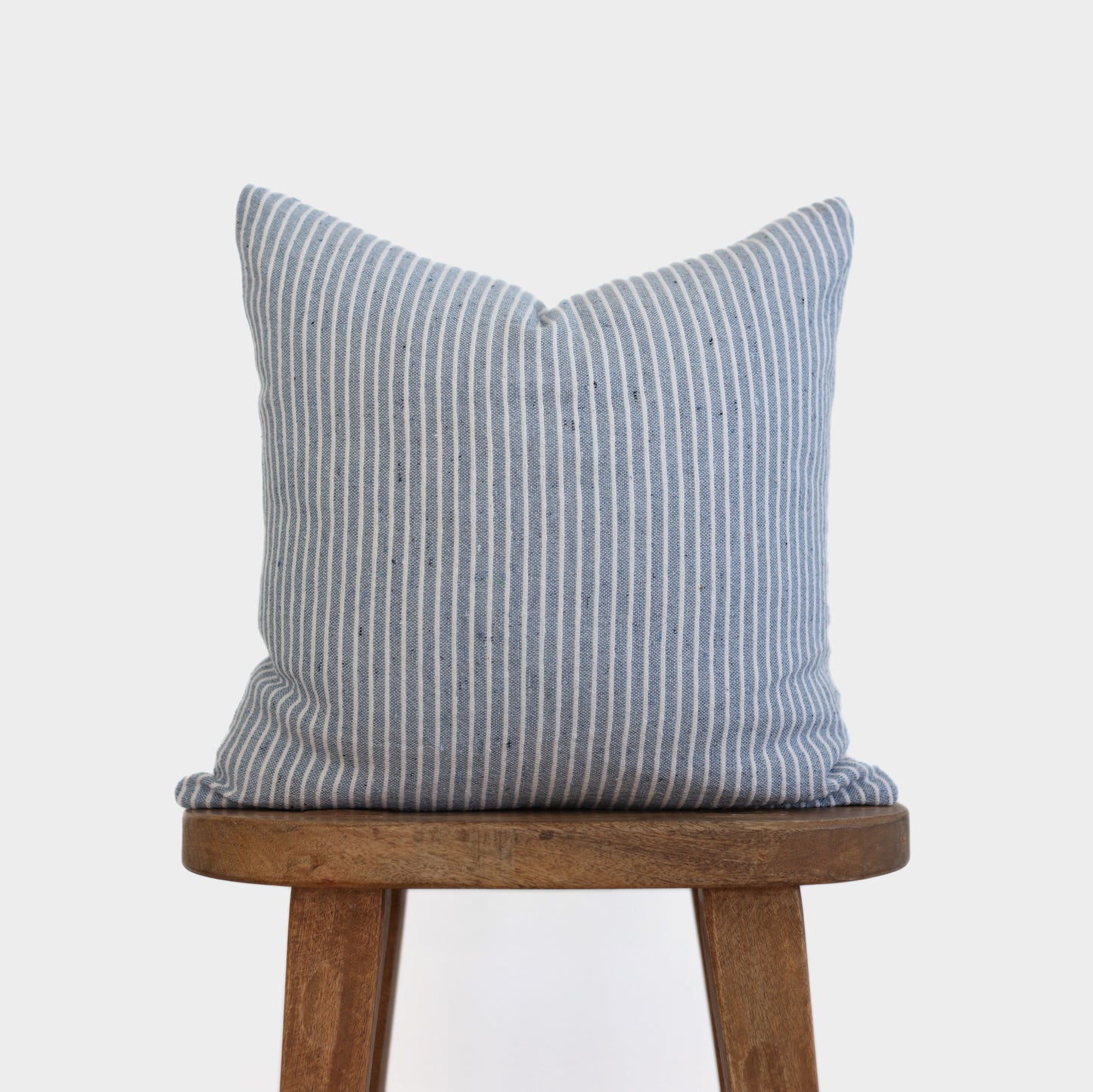 Blue and white striped throw pillow on wooden stool.