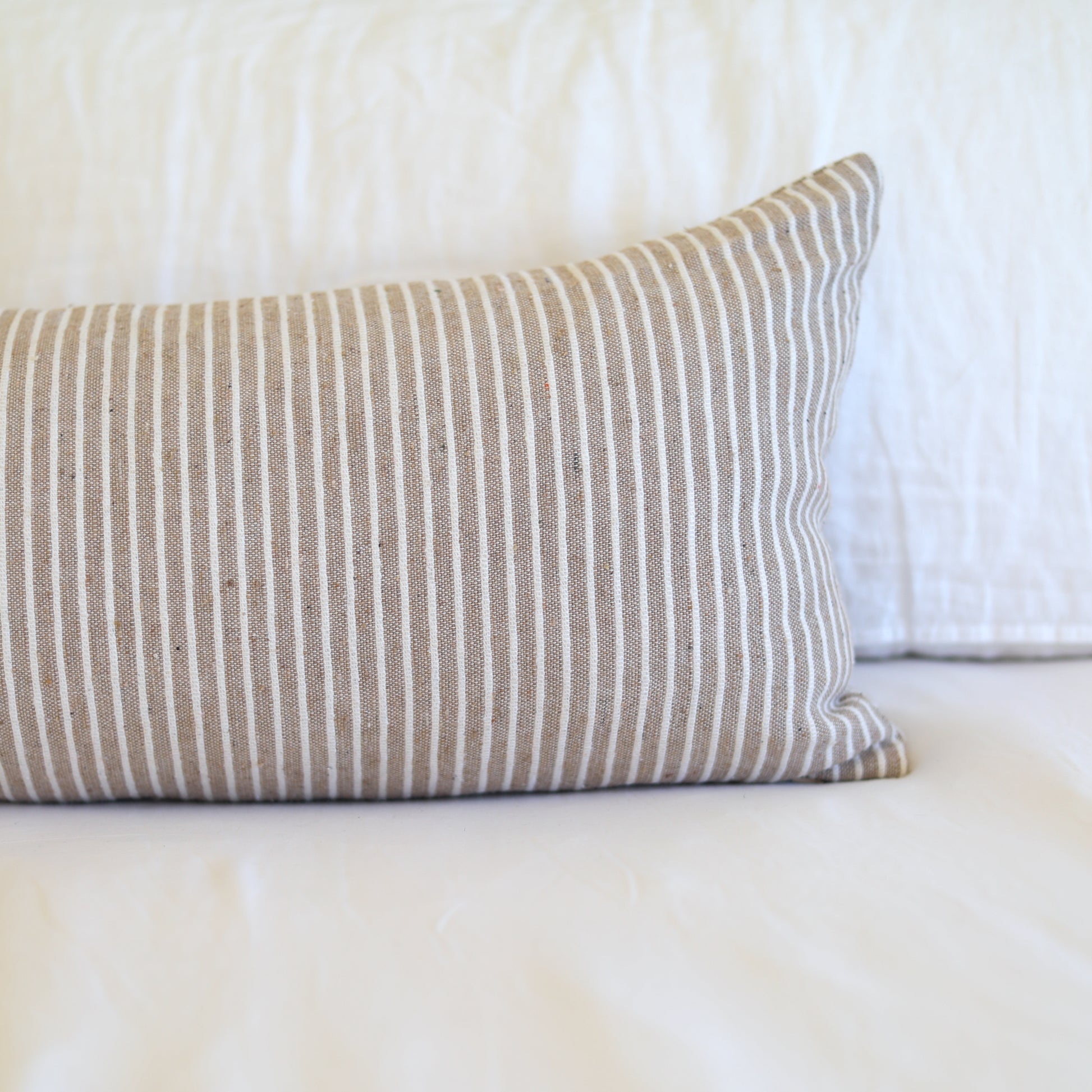Tan and white striped lumbar pillow with vertical ribbed texture on white bedding.
