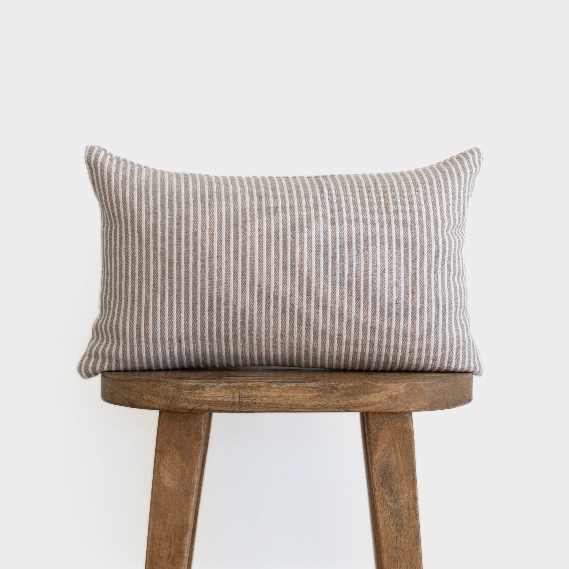 Tan and white striped rectangular lumbar pillow displayed on a wooden stool.