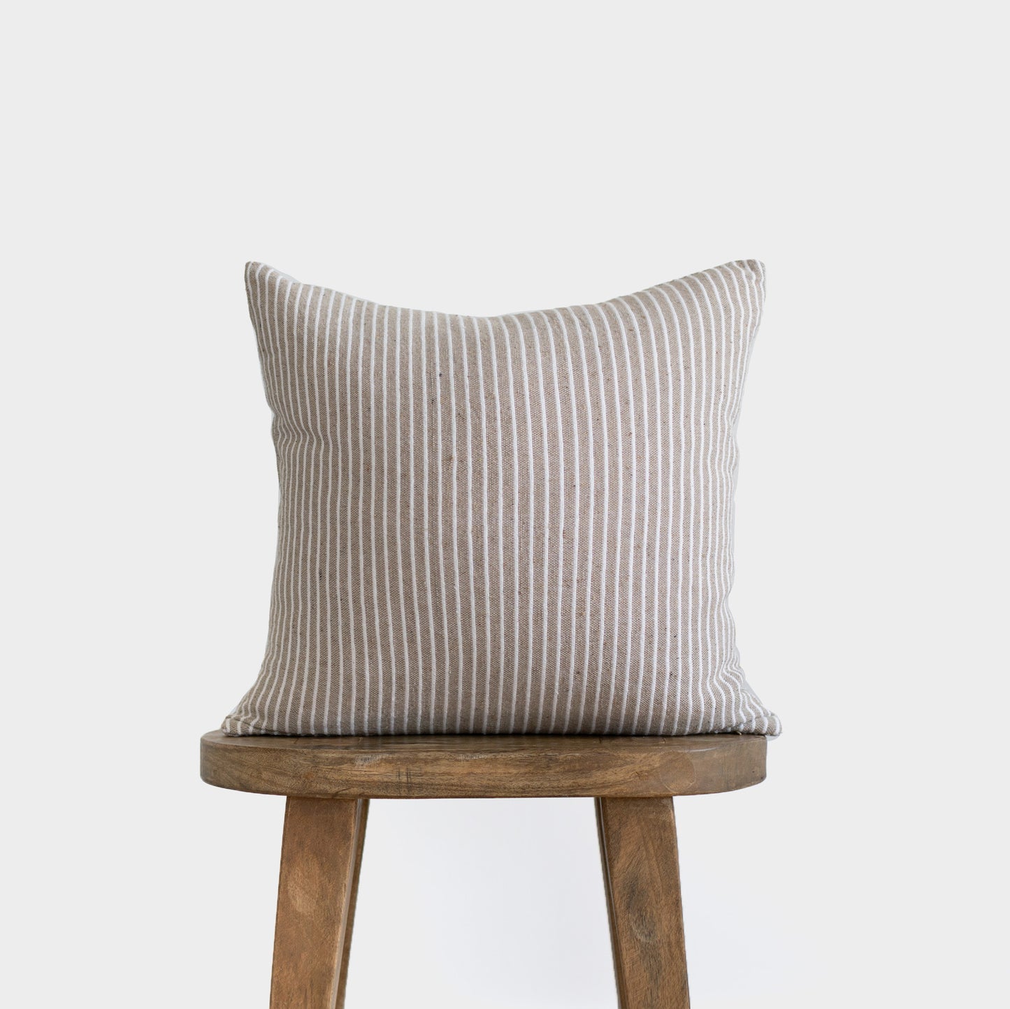 Tan and white striped square pillow displayed on a wooden stool.